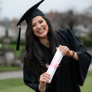 Image of a student holding a diploma dressed in graduation cap and gown